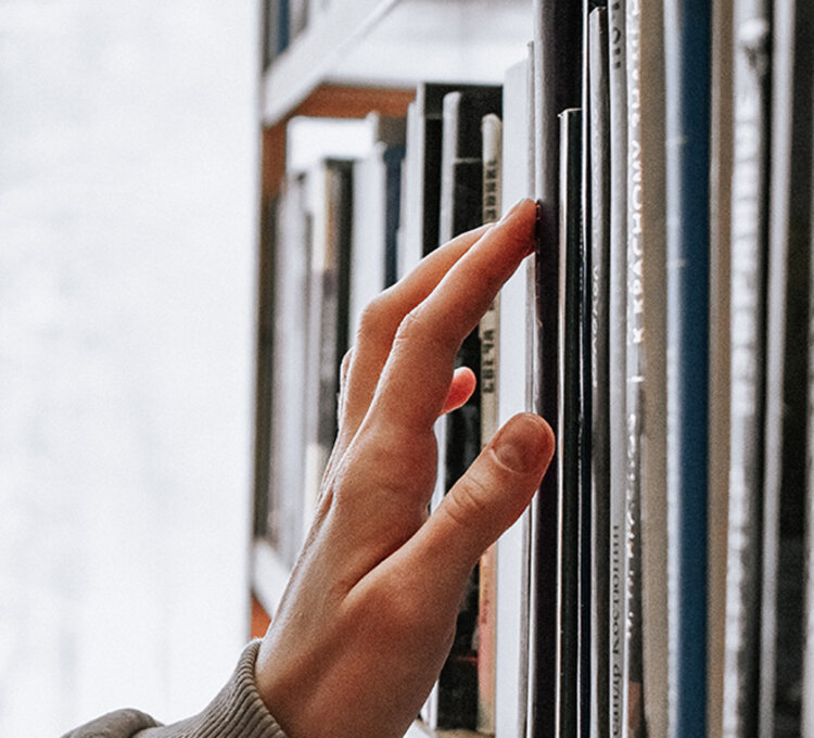 Buchentnahme am Regal Hand zieht ein Buch aus einem vertikalen Regal in der Bibliothek.